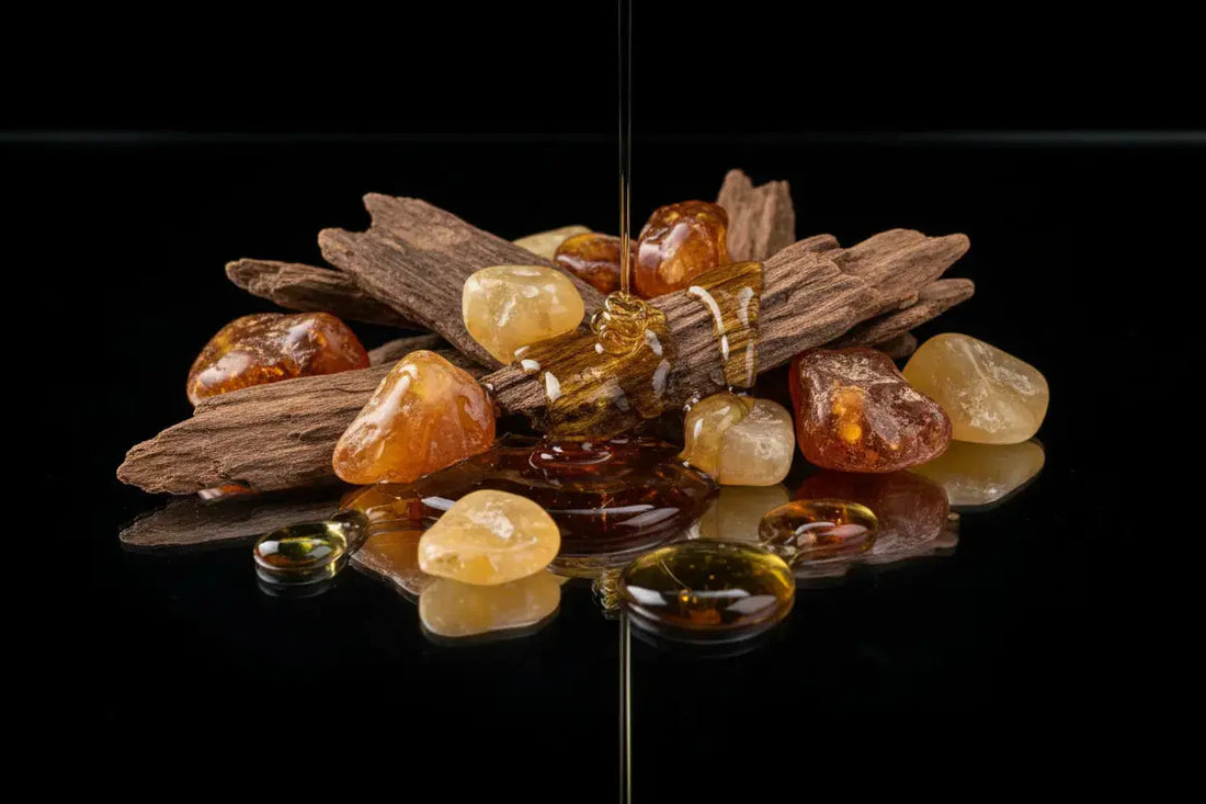 A collection of amber stones and oud wood pieces, reflecting on a glossy black surface, showcasing rich golden hues.